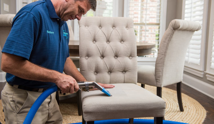 Expert cleaning an upholstered chair using cleaning equipment